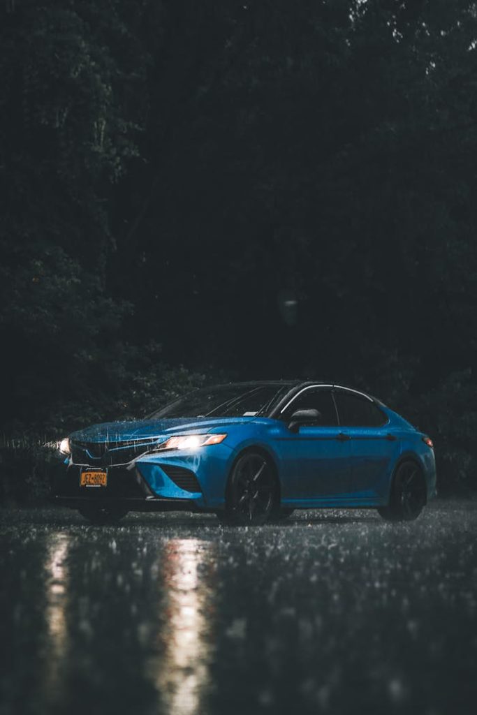 A striking image of a blue car parked in the rain on a dark night.